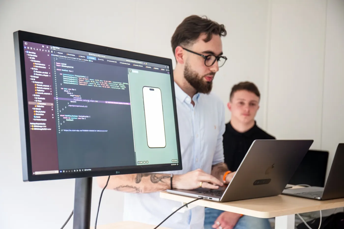 Two developers working together in front of a screen and a laptop