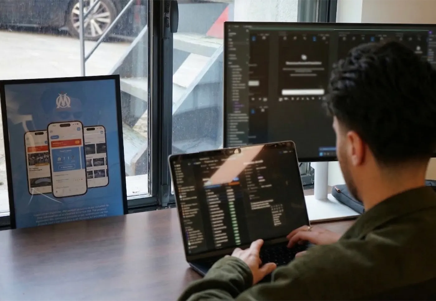 A developer at work on a laptop, next to framed app mock-ups